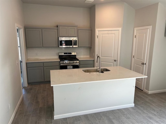 kitchen featuring sink, appliances with stainless steel finishes, a kitchen island with sink, and gray cabinetry