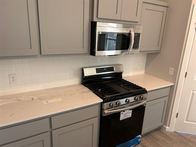 kitchen with decorative backsplash, stainless steel appliances, gray cabinetry, and light stone counters