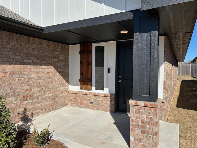 entrance to property with brick siding, board and batten siding, and fence