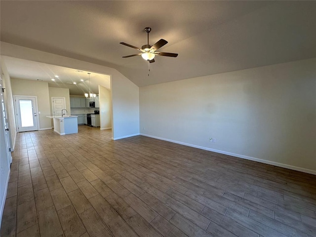 unfurnished living room featuring lofted ceiling, baseboards, dark wood-style flooring, and ceiling fan with notable chandelier