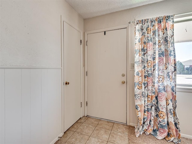 doorway to outside featuring wainscoting, a textured ceiling, and light tile patterned flooring