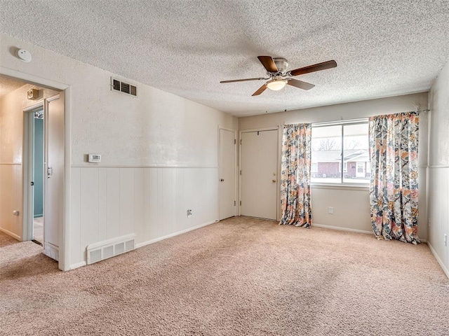 carpeted spare room featuring ceiling fan, visible vents, a textured ceiling, and wainscoting