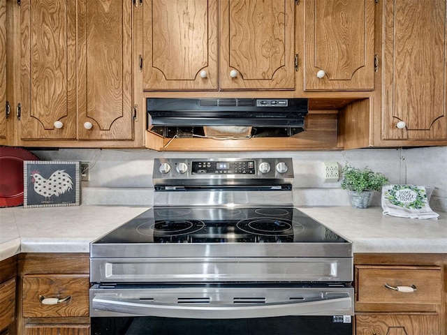 kitchen with under cabinet range hood, light countertops, electric stove, and brown cabinetry