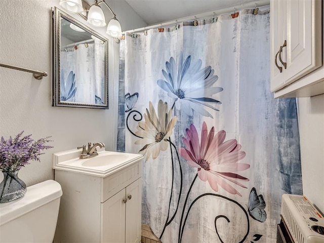 bathroom featuring toilet, heating unit, a textured wall, and vanity