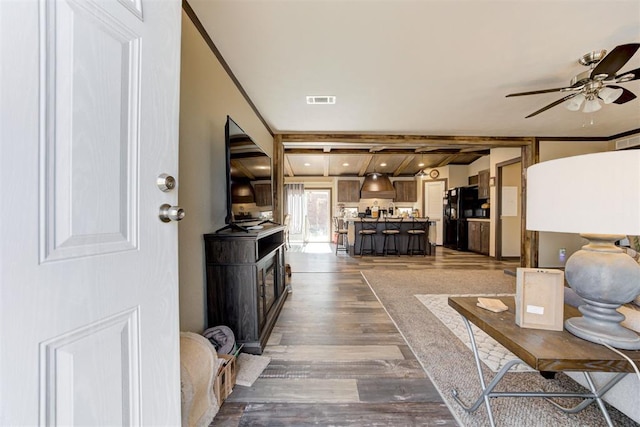 living area featuring visible vents, a ceiling fan, ornamental molding, dark wood-style floors, and beamed ceiling