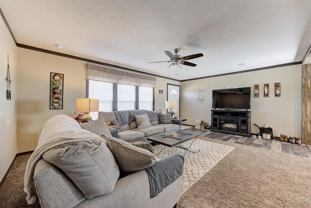 living area featuring ornamental molding, a glass covered fireplace, ceiling fan, and baseboards