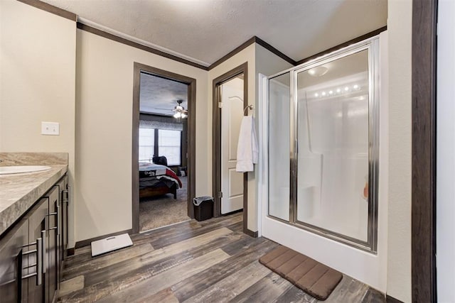 bathroom with crown molding, wood finished floors, a textured ceiling, a shower stall, and ensuite bath