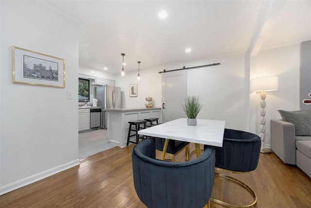 dining space featuring light hardwood / wood-style flooring, crown molding, and a barn door