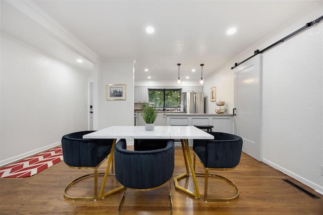 dining room featuring sink, light hardwood / wood-style flooring, crown molding, and a barn door