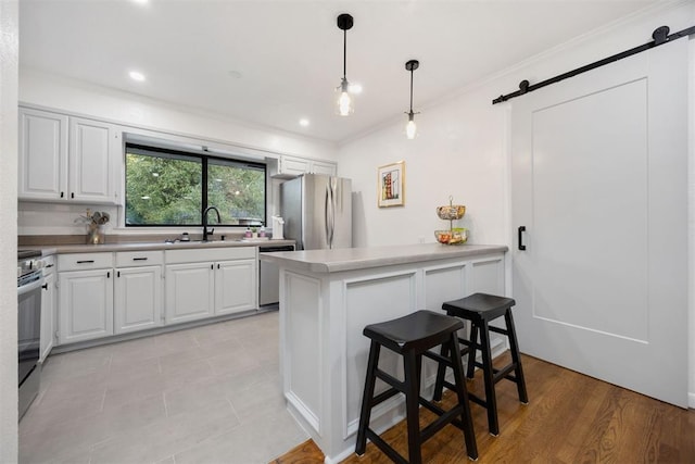 kitchen with white cabinetry, stainless steel appliances, a barn door, sink, and a breakfast bar area