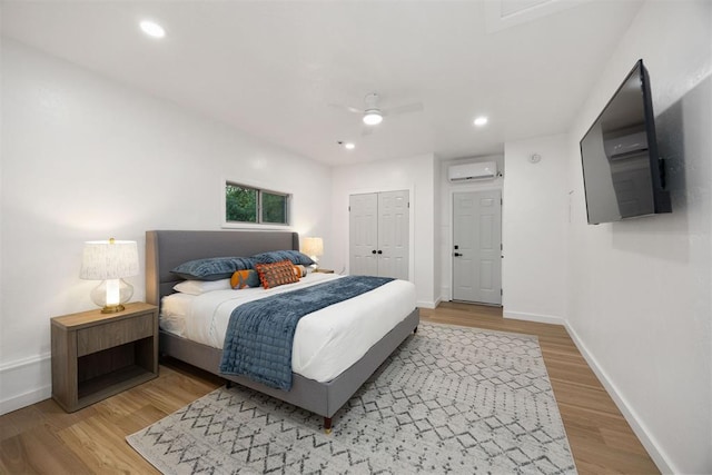 bedroom with ceiling fan, light wood-type flooring, a wall mounted AC, and a closet