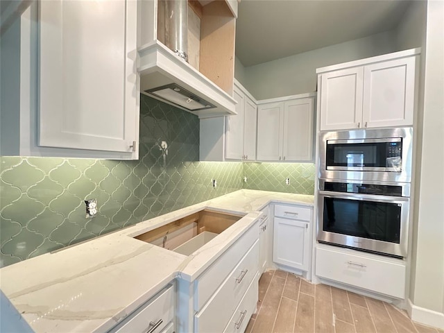 kitchen with decorative backsplash, white cabinetry, light stone counters, and custom exhaust hood