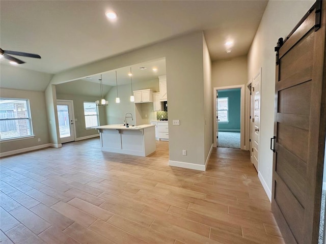 kitchen with a kitchen island with sink, decorative light fixtures, open floor plan, a barn door, and light wood finished floors