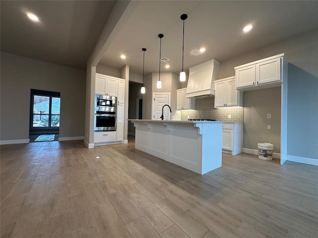 kitchen featuring white cabinetry, a center island with sink, stainless steel appliances, and premium range hood