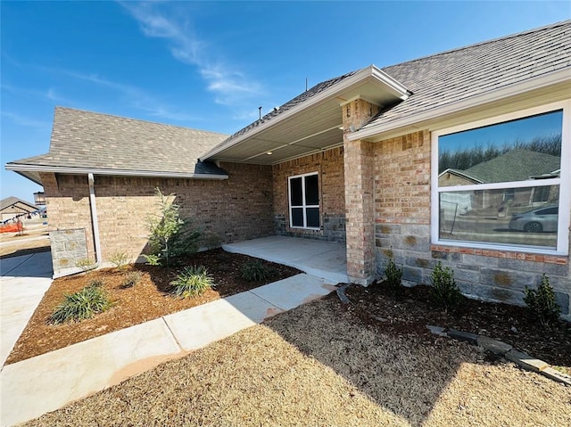 property entrance with a patio, brick siding, and roof with shingles