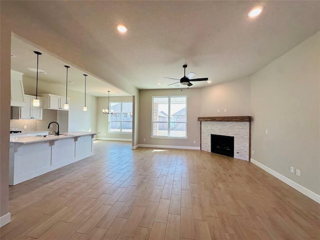 unfurnished living room with light wood finished floors, baseboards, ceiling fan, recessed lighting, and a sink