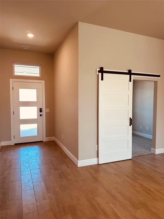 entrance foyer featuring a barn door, visible vents, baseboards, and wood finished floors