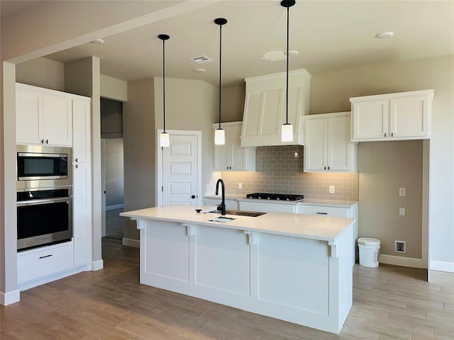 kitchen with stainless steel appliances, backsplash, a sink, visible vents, and light wood-style flooring
