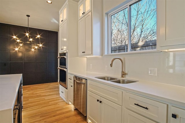 kitchen featuring pendant lighting, white cabinetry, sink, stainless steel appliances, and light hardwood / wood-style flooring