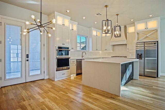 kitchen featuring premium range hood, appliances with stainless steel finishes, white cabinetry, hanging light fixtures, and a center island