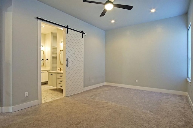 carpeted empty room featuring ceiling fan, a barn door, and sink