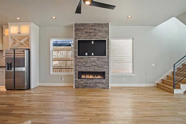 unfurnished living room featuring a stone fireplace, ceiling fan, and light wood-type flooring