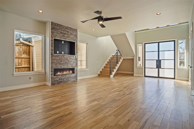 unfurnished living room with ceiling fan, a stone fireplace, and light hardwood / wood-style floors