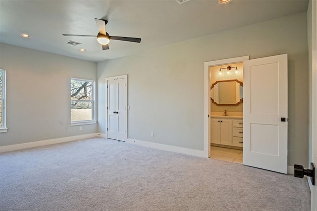 unfurnished bedroom featuring ceiling fan, light colored carpet, ensuite bathroom, and a closet