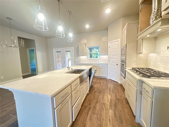 kitchen with premium range hood, stainless steel appliances, sink, white cabinetry, and a kitchen island with sink