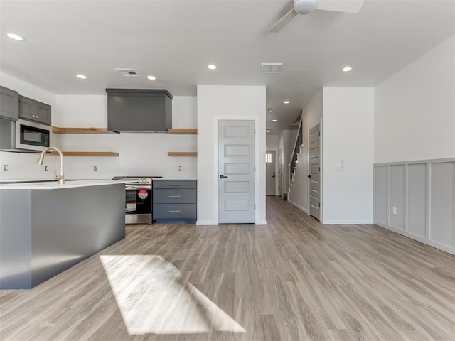 kitchen with black microwave, wall chimney range hood, light hardwood / wood-style floors, sink, and stainless steel range