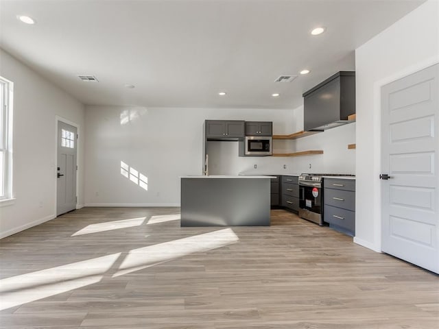 kitchen with gray cabinetry, stainless steel appliances, a kitchen island, light hardwood / wood-style floors, and wall chimney exhaust hood