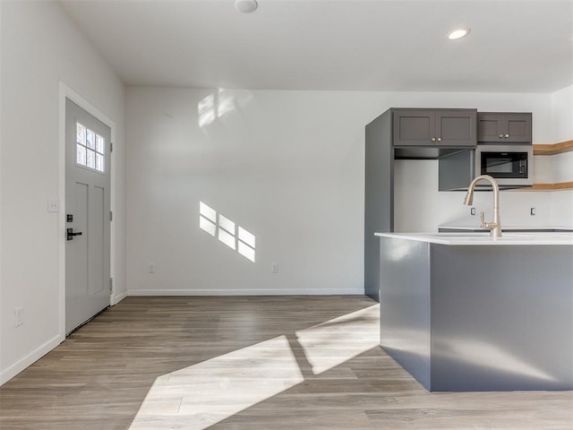kitchen with light wood-type flooring, stainless steel microwave, baseboards, and open shelves