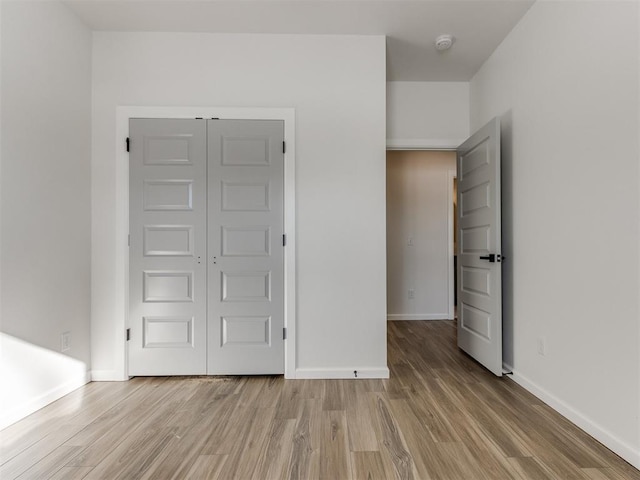 unfurnished bedroom with a closet, baseboards, and light wood finished floors