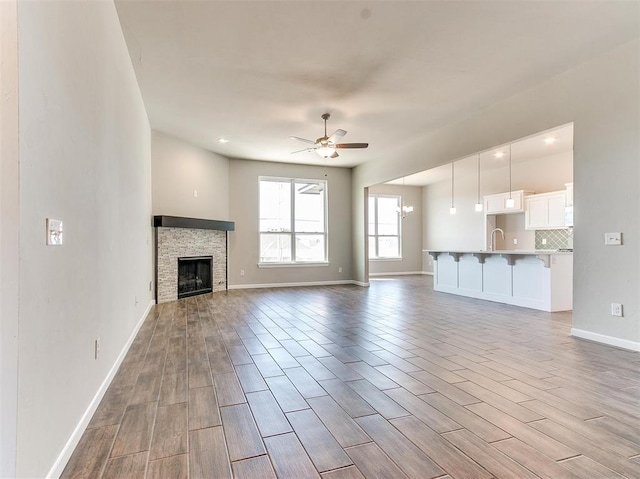 unfurnished living room with ceiling fan with notable chandelier, sink, and a stone fireplace