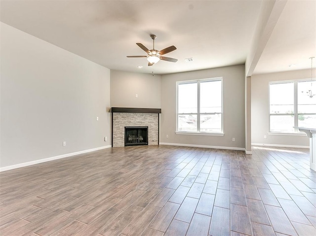 unfurnished living room with ceiling fan with notable chandelier, light wood-type flooring, and a fireplace