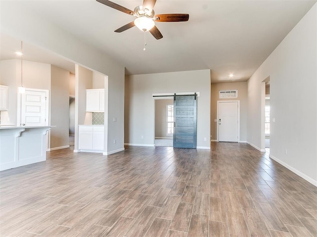 unfurnished living room featuring light hardwood / wood-style floors, ceiling fan, and a barn door