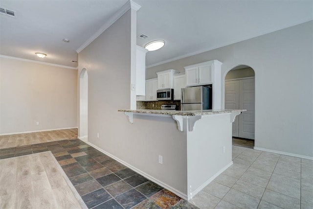 8016 Heather Glen Dr, Yukon, OK 73099 - kitchen featuring white cabinets, arched walkways, appliances with stainless steel finishes, light stone counters, and a breakfast bar area