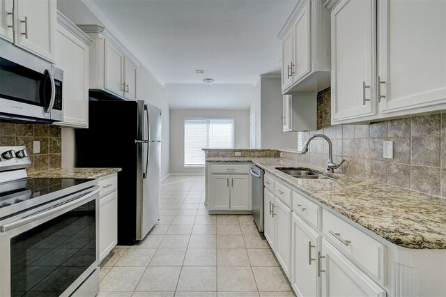 8016 Heather Glen Dr, Yukon, OK 73099 - kitchen featuring light stone counters, light tile patterned floors, a sink, a peninsula, and appliances with stainless steel finishes