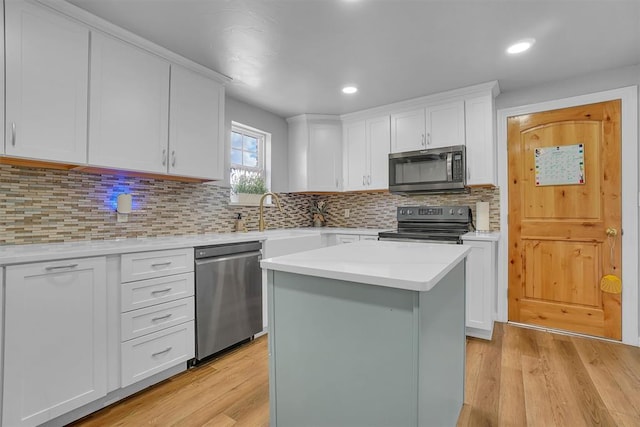 kitchen featuring stainless steel appliances, white cabinets, light hardwood / wood-style floors, a kitchen island, and sink