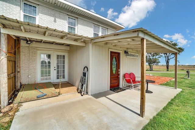 view of exterior entry featuring french doors, a lawn, and a patio area