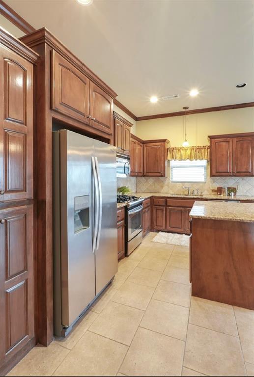 kitchen with appliances with stainless steel finishes, pendant lighting, ornamental molding, and tasteful backsplash