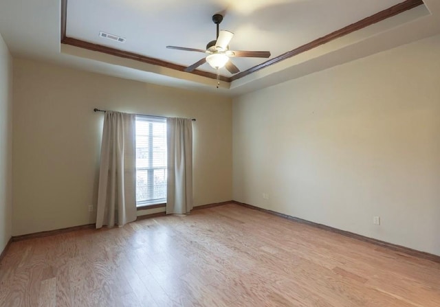 spare room with a tray ceiling, ceiling fan, light wood-type flooring, and ornamental molding