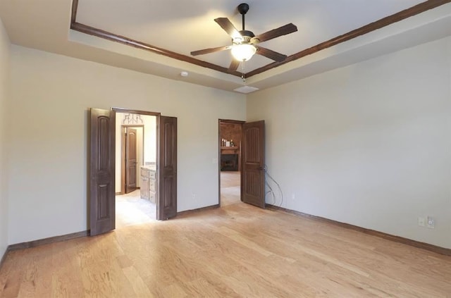 unfurnished bedroom with light hardwood / wood-style flooring, ceiling fan, and a raised ceiling