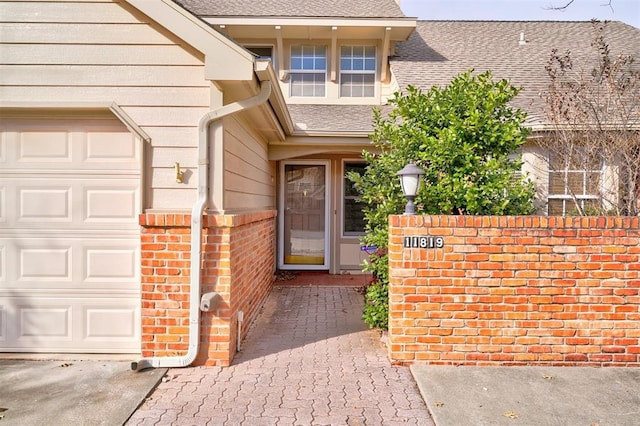 entrance to property with an attached garage, brick siding, and roof with shingles