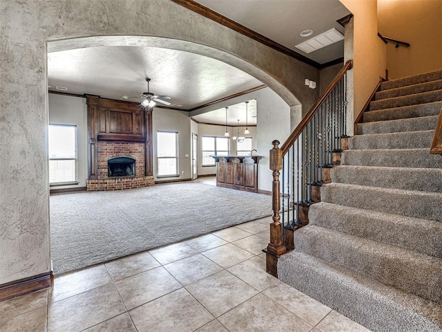 unfurnished living room with ceiling fan, crown molding, light colored carpet, and a fireplace