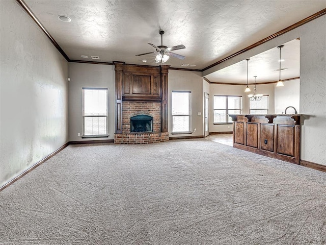 unfurnished living room with a brick fireplace, light colored carpet, ornamental molding, a textured ceiling, and ceiling fan with notable chandelier