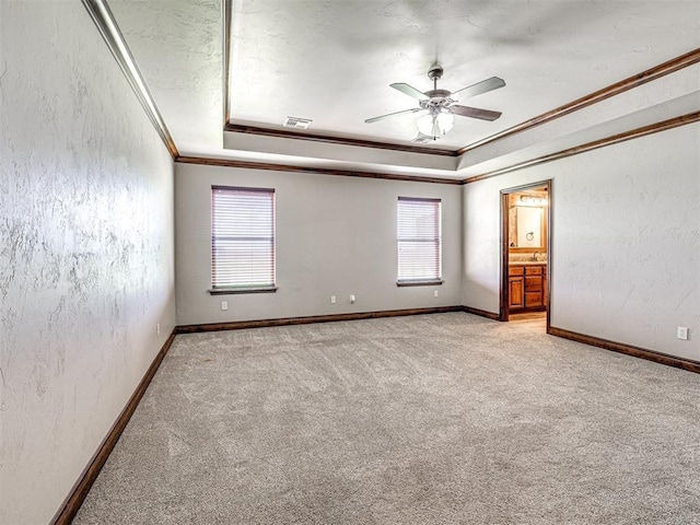 carpeted spare room with a tray ceiling, ornamental molding, and ceiling fan