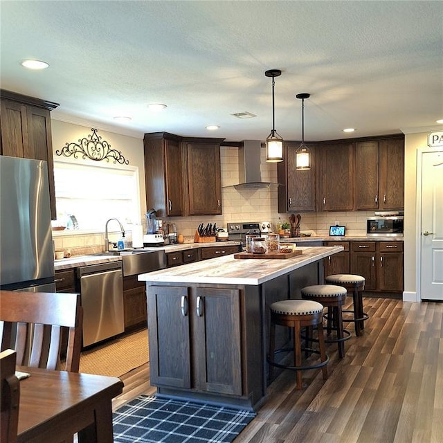 kitchen with wall chimney exhaust hood, appliances with stainless steel finishes, a center island, light countertops, and pendant lighting