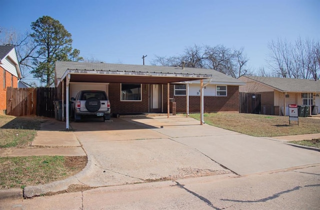 single story home featuring brick siding, an attached carport, driveway, and fence