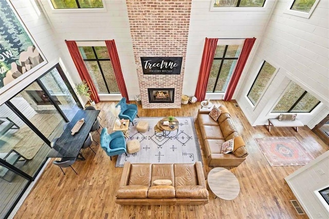 living area with plenty of natural light, a brick fireplace, wood finished floors, and visible vents